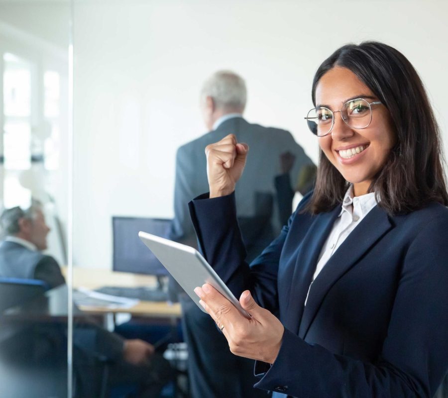 happy-female-professional-glasses-suit-holding-tablet-making-winner-gesture-while-two-businessmen-working-glass-wall-copy-space-communication-concept